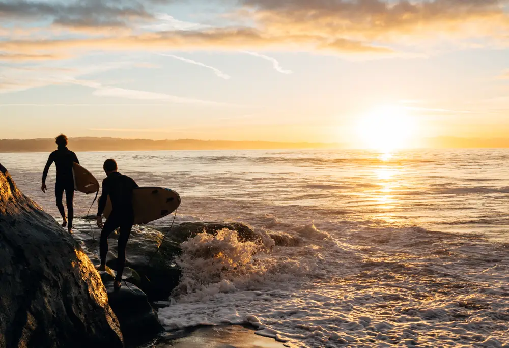 Two surfers with boards in Santa Cruz at sunrise for an article showing the best beaches in California