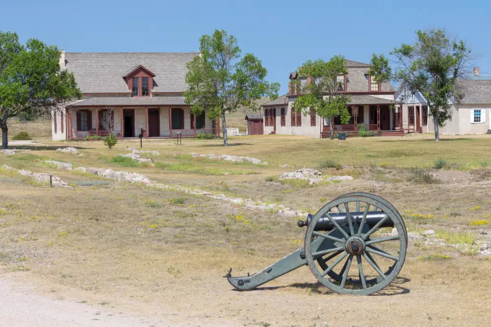 Picture of a cannon in a dirt field outside of a couple old barracks buildings in one of Wyoming's best places to visit, Fort Laramie