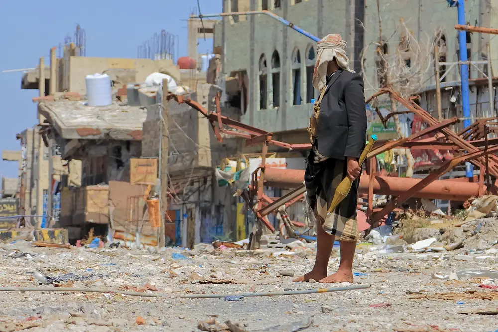 Man stands with a rocket shell in his hand and surveying the damage in the bombed-out city of Taiz