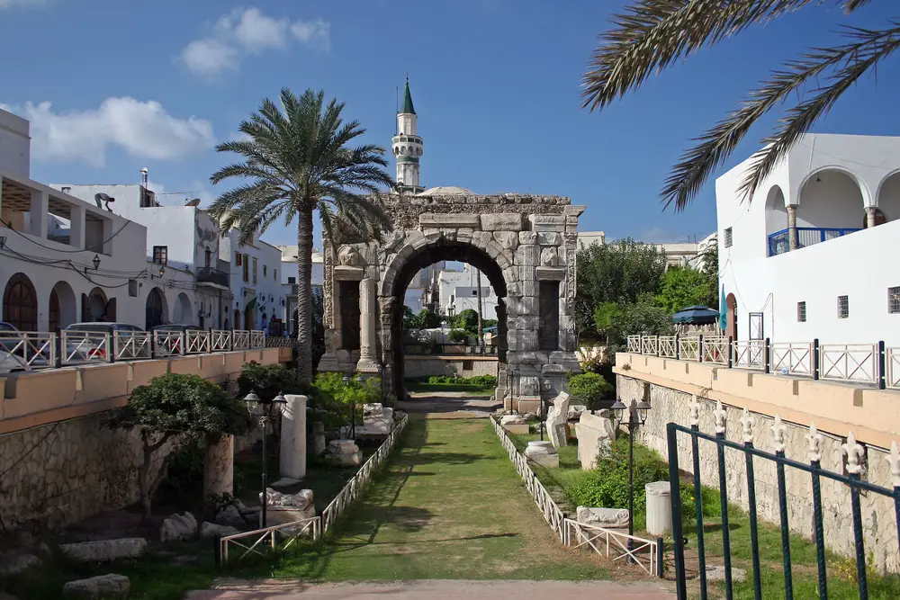 The Arch of Roman emperor Marcus Aurelius pictured for a piece titled Is Libya Safe to Visit with the ruins in the background between large trees and buildings