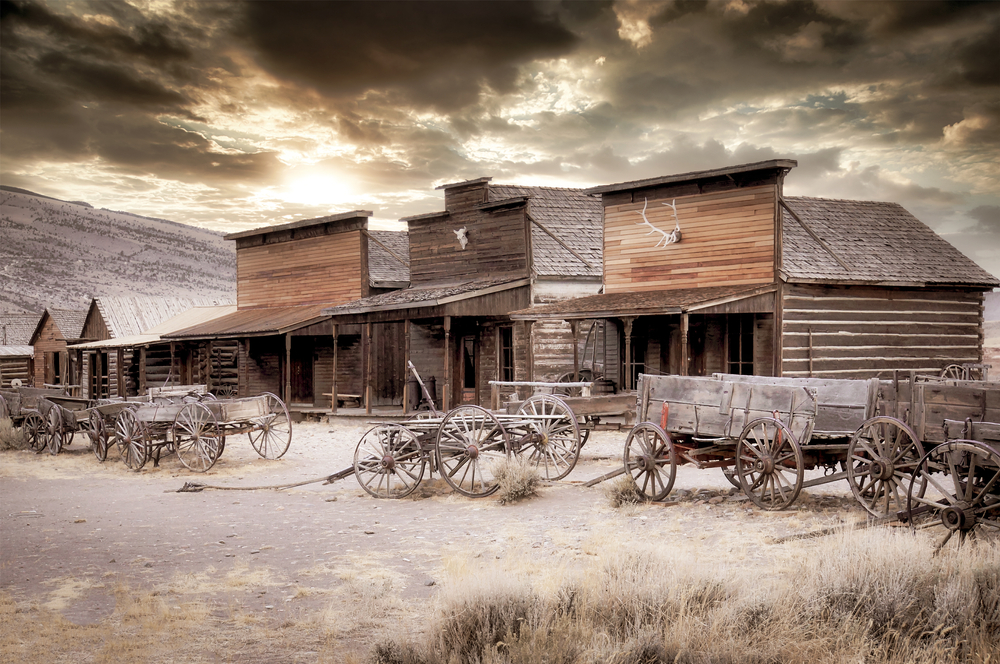 Old Trail Town στο Cody, μια κορυφαία επιλογή για μέρη που πρέπει να επισκεφτείτε στο Wyoming, που απεικονίζεται με εγκαταλελειμμένα ξύλινα κτίρια δίπλα σε παλιά καροτσάκια με άλογα