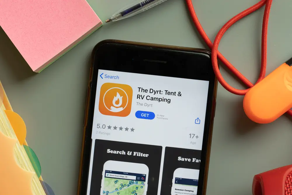The Dyrt camping app shown in the App Store on a smartphone is one of the best trip planning apps to see campsite reviews and find open sites around the U.S.