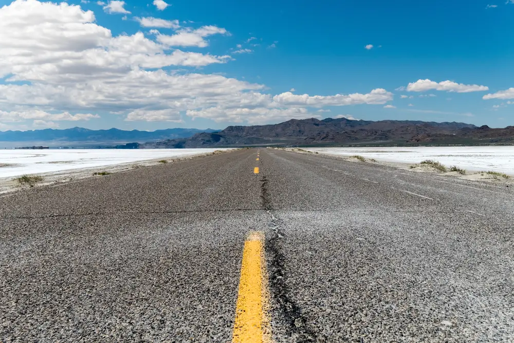 Empty road with yellow lines showing the best time to visit the Bonneville Salt Flats with blue skies overhead