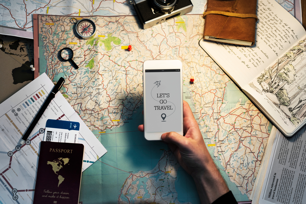 Hand holding a smartphone reading Let's go travel over a map with travel documents on the table for a piece showing the best travel planning apps