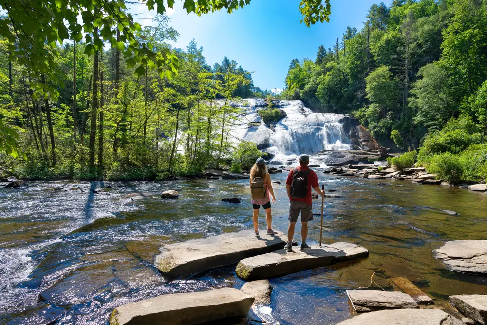 For a guide to the best time to visit Asheville NC, a couple standing on a rock overlooking the waterfall