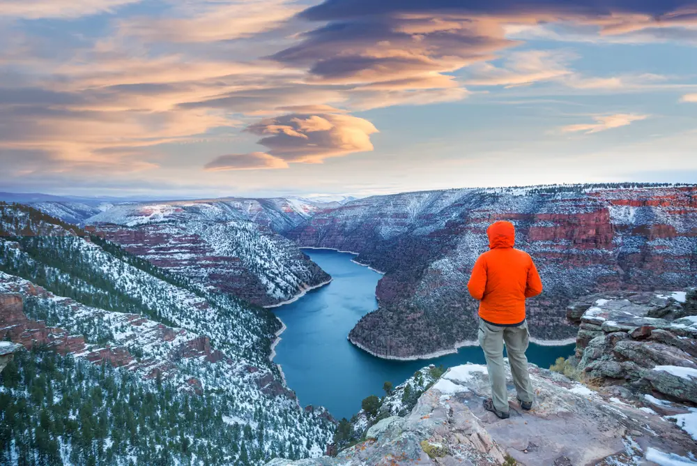 For a piece on the best places to visit in Wyoming, a man in a red coat with his hood up on the edge of a cliff overlooking the winter scene below at the Flaming Gorge recreation area