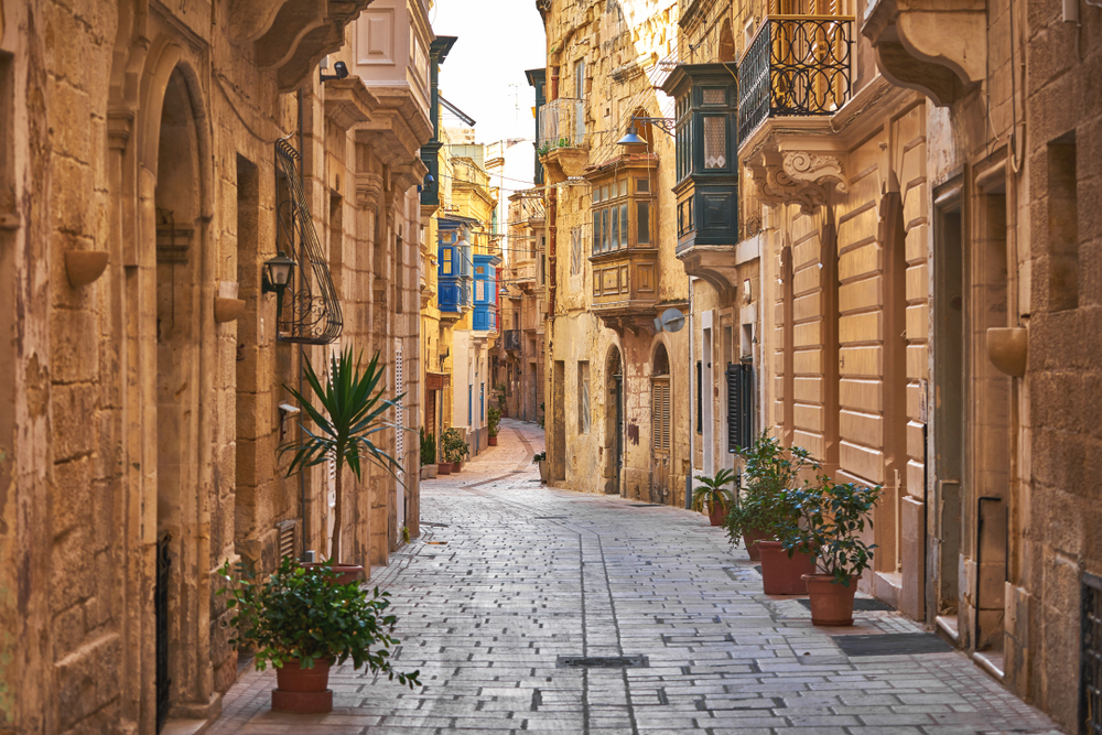 Picturesque cobblestone street running down the middle of several tan buildings for a piece titled Is Malta Safe to Visit