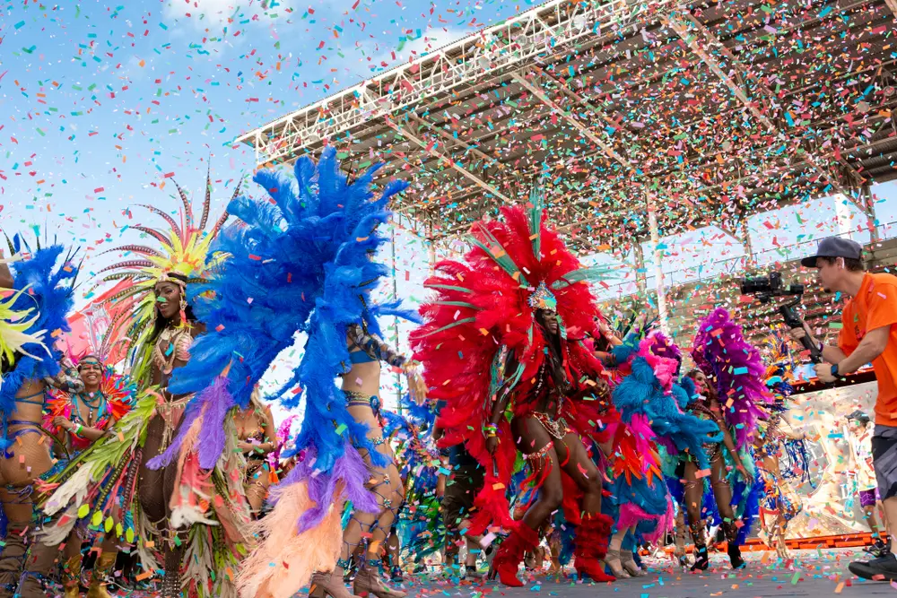 Carnival parade participants in bright feathers dance with confetti falling during the overall best time to visit Trinidad