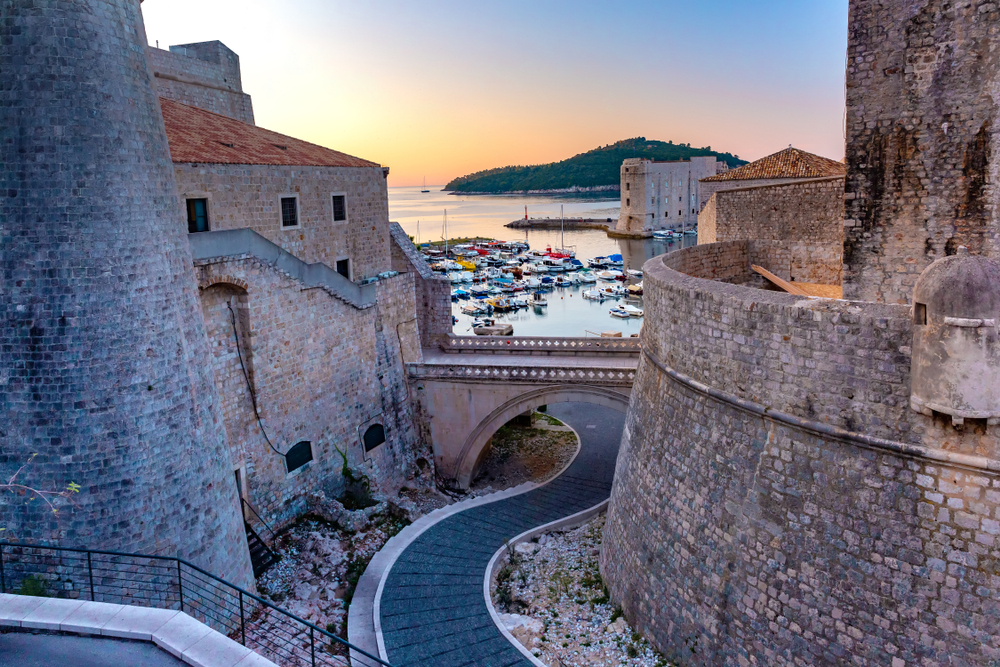 Winding path leads under a bridge down to the water in Old Harbour at sunset to indicate the best time to visit Dubrovnik for great weather