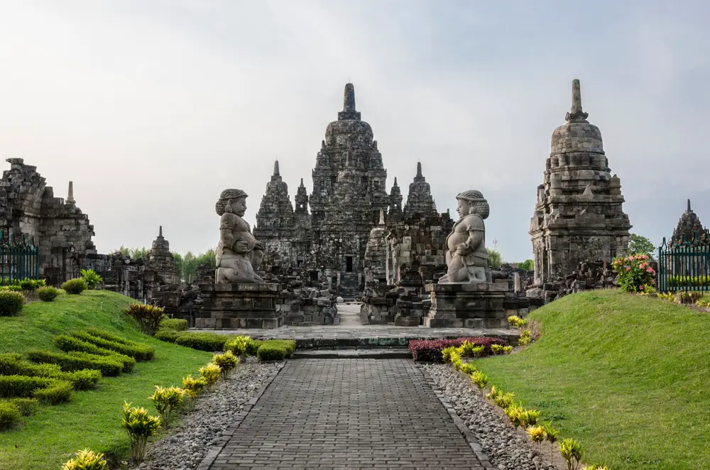 Photo of the outside of the Prambanan Temple pictured on a foggy day between two grassy berms