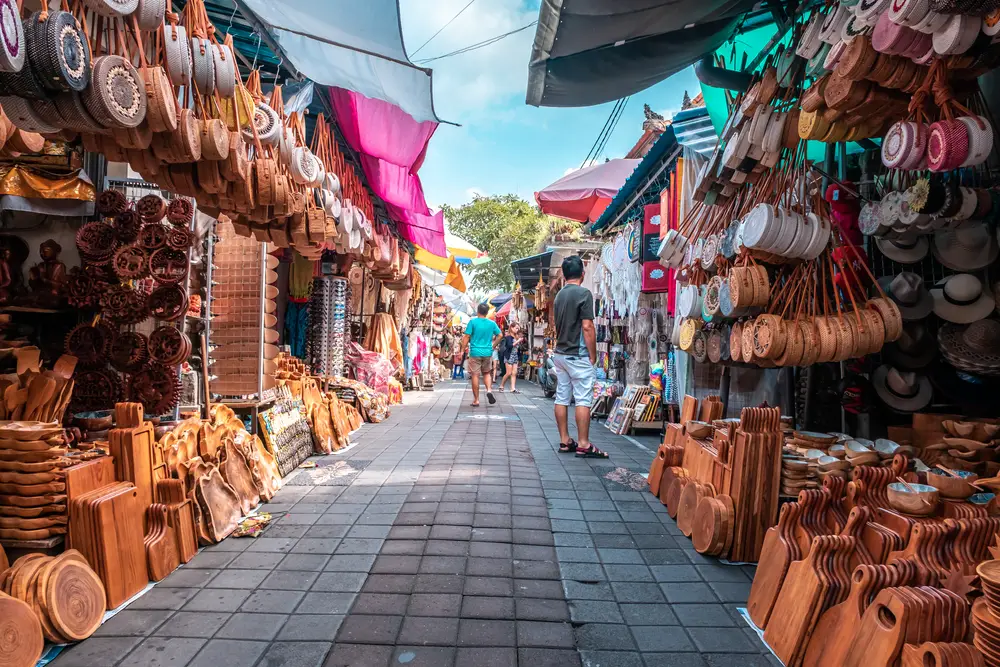 For a piece titled Is Indonesia Safe to Visit, a street market with wooden goods for sale pictured in the tourist area of Ubud
