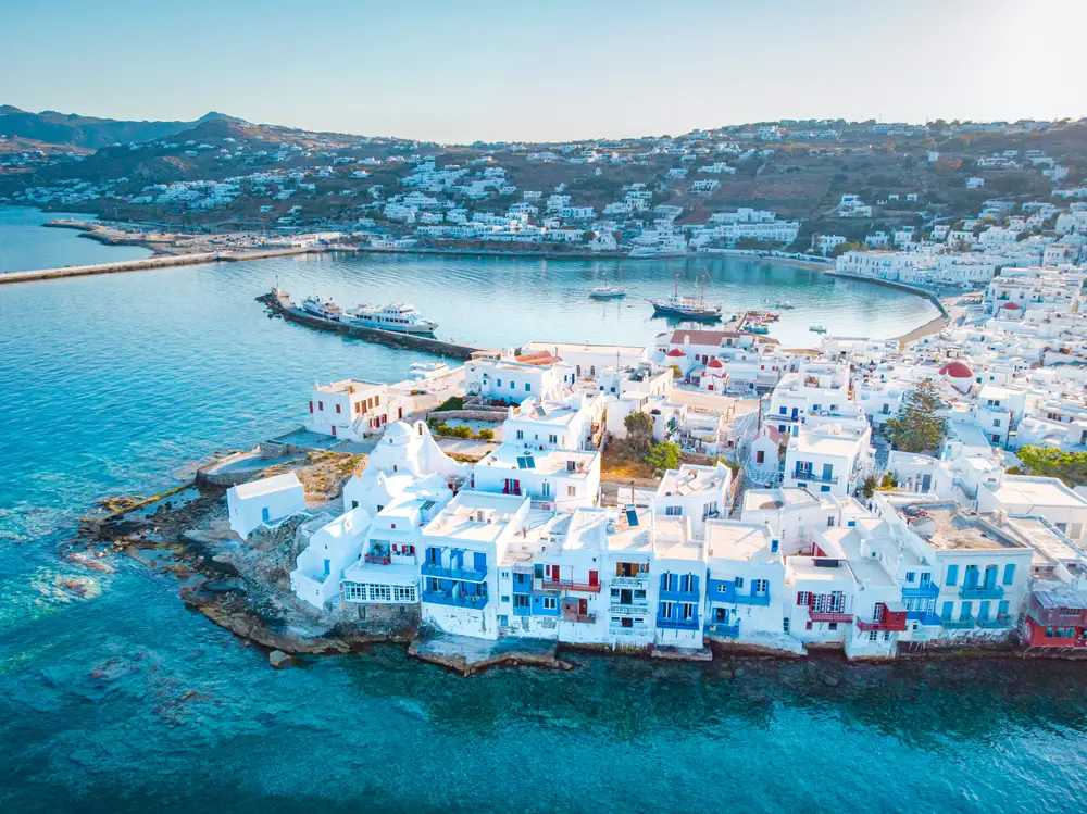 Aerial view of the whitewashed limestone village with hills in the distance to indicate why you should visit Mykonos