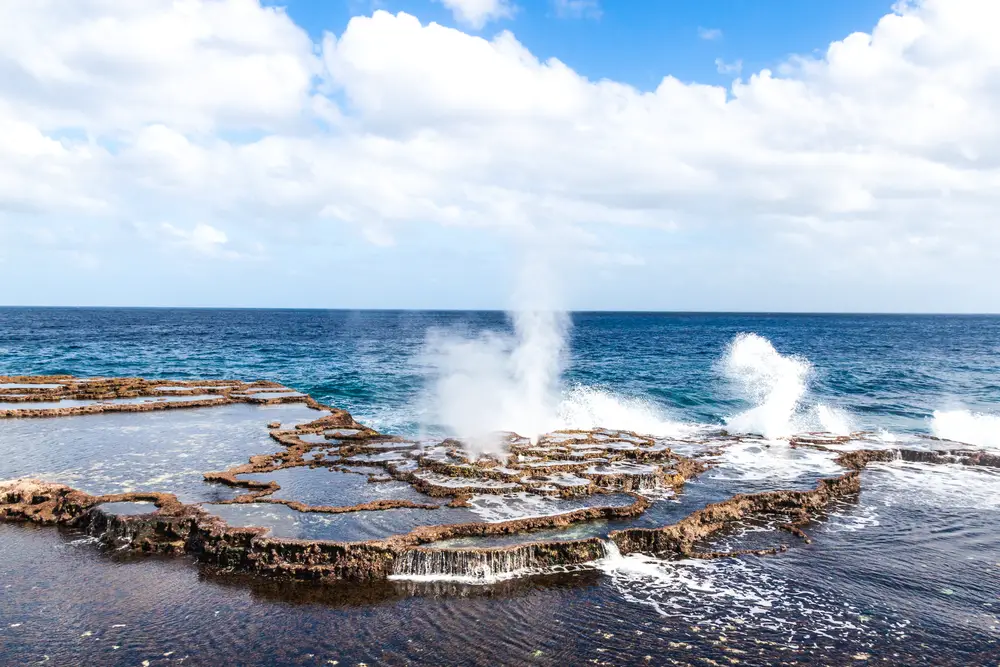 Blowholes or sea geysers along the Tongan coast as waves crash against the rocks during the best time to visit Tonga with clouds in the sky