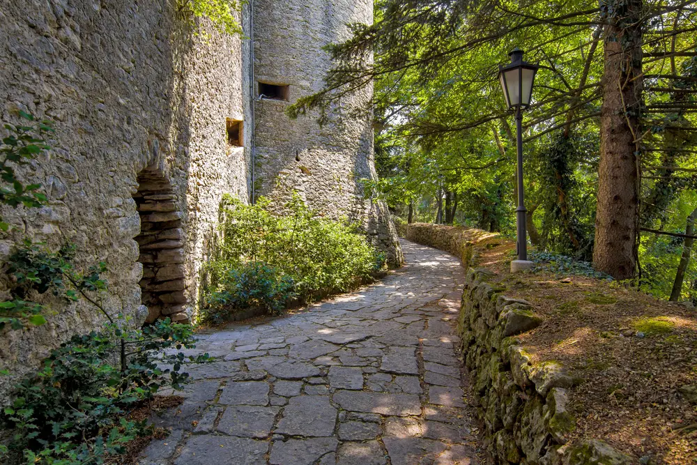 Dappled sunlight hits a cobblestone path around the De La Fratta tower during the overall best time to visit San Marino from May to July