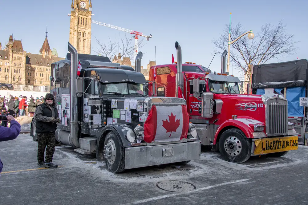 Ottawa Freedom Convoy pictured with Canadian flags on the front of the trucks and the drivers standing next to the trucks