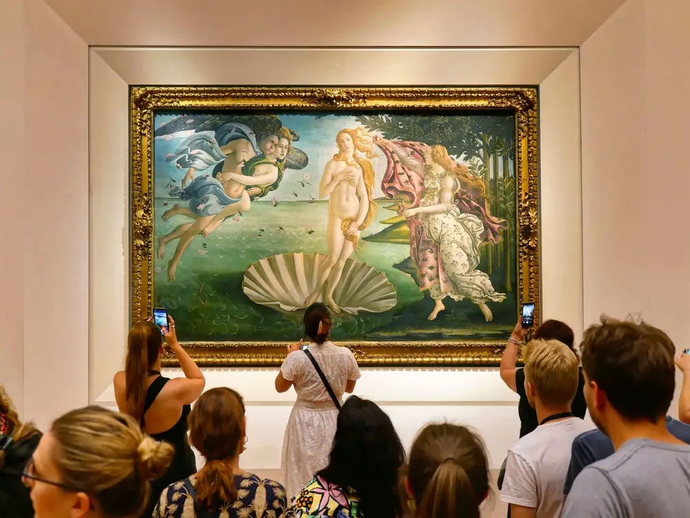 Tourists gather around the Birth of Venus painting by Botticelli in the Uffizi Gallery during the best time to visit Florence in the peak summer season