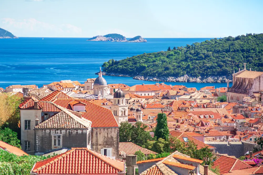 Aerial view of buildings and homes in the Old City during the best time to visit Dubrovnik with tiled roofs and green islands in the distance