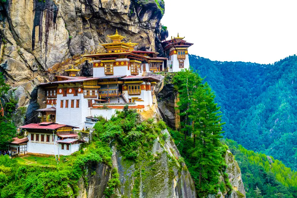 Cliffside monastery pictured with greenery and moss on the rocks for a piece titled is Bhutan safe to travel to
