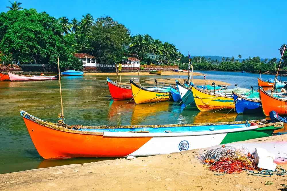 For a piece titled Is It Safe to Travel to Goa, a bunch of colorful fishing boats are seen on the water 
