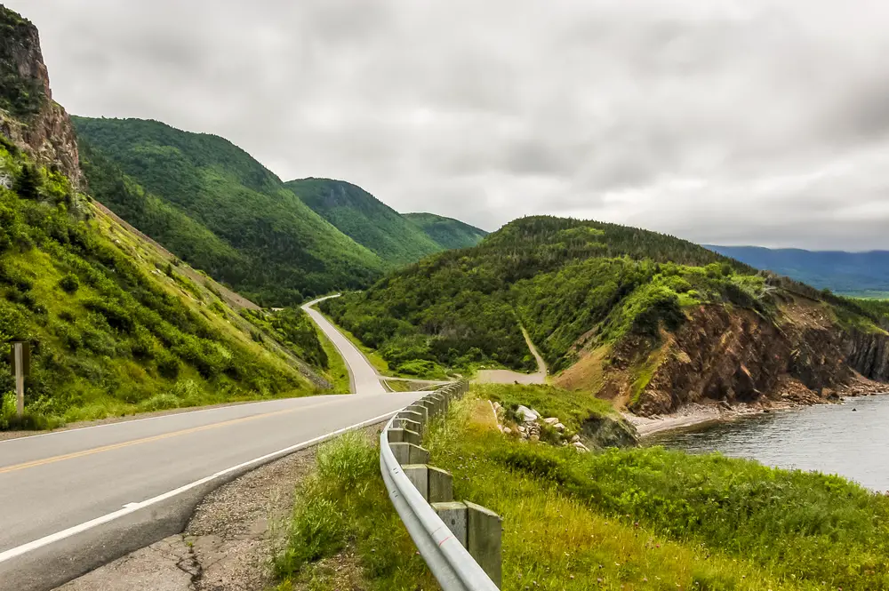 Photo of the green grass on either side of the winding road on Cape Breton Island in Nova Scotia during the best time to go