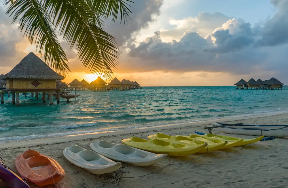 Ηλιοβασίλεμα πάνω από τις καλύβες σε μια παραλία στη Μπόρα Μπόρα που απεικονίζεται για ένα κομμάτι με τίτλο Bora Bora Safe to Travel to