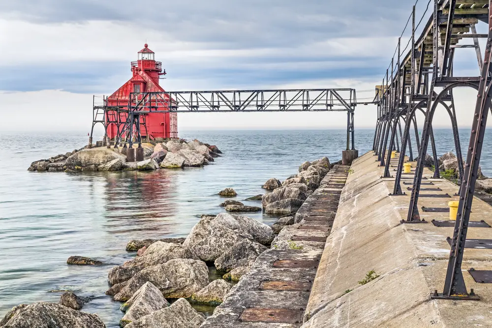 The famous red lighthouse of Sturgeon Bay pictured on a cloudy day with an elevated metal platform on the right side