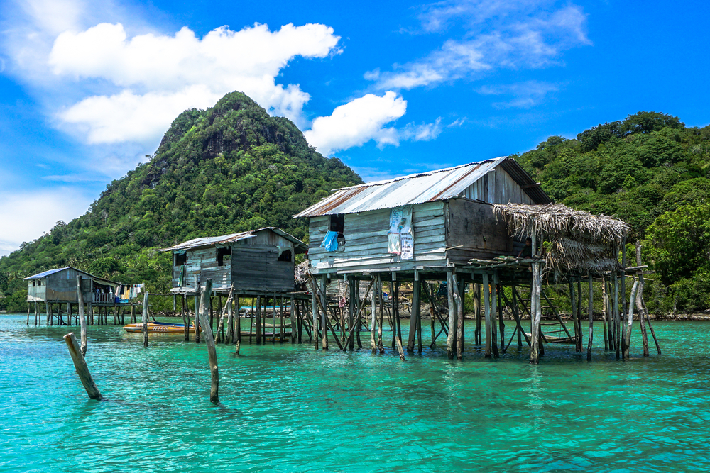 Neat blue homes on stilts pictured above teal water offshore from Mabul Bodgaya