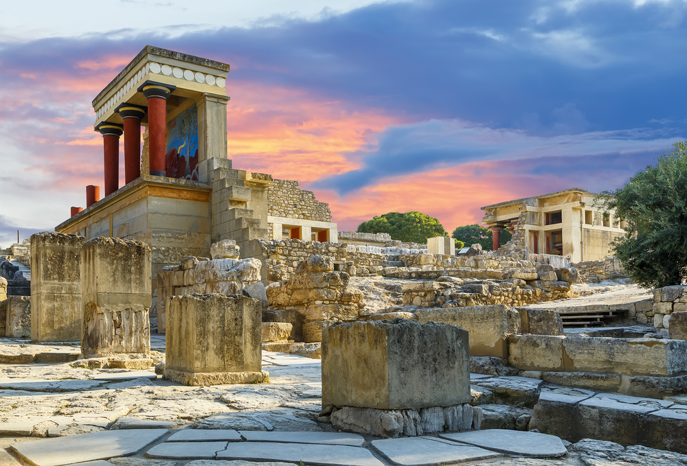 Picturesque view of the old ruins of the Knossos Palace in Crete pictured during the best time to visit with a pink and orange dusk sky overhead