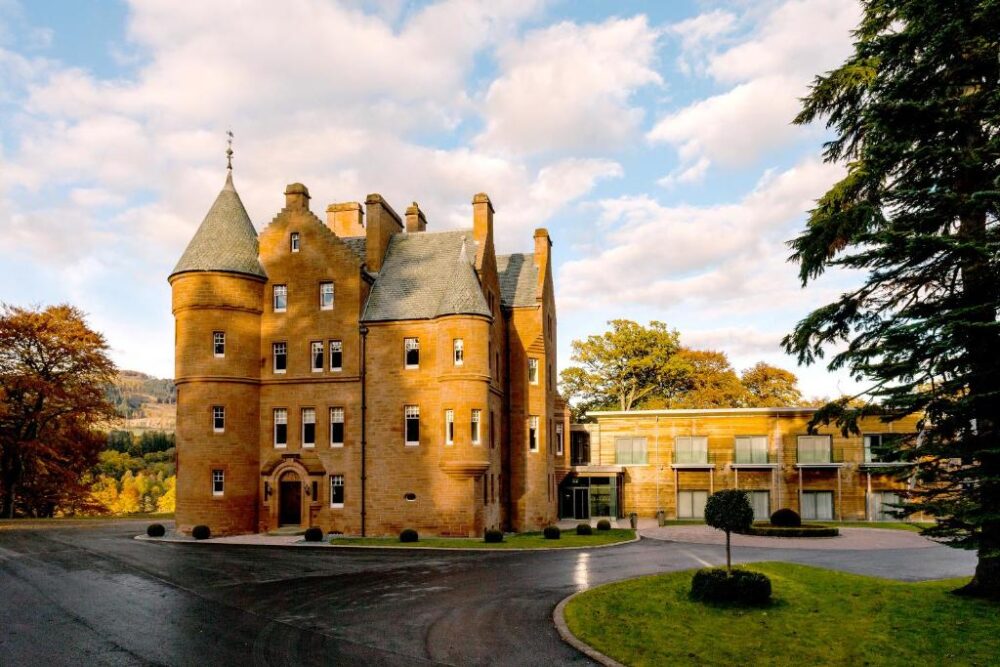 Fonab Hotel, one of the best castle hotels in Scotland, picture with its orange brick in a gorgeous scene towering over the black drive