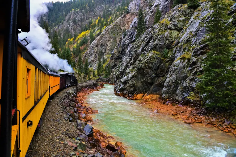Old steam-powered train making its way through the mountains next to the Animas River during the overall best time to visit Durango, Colorado