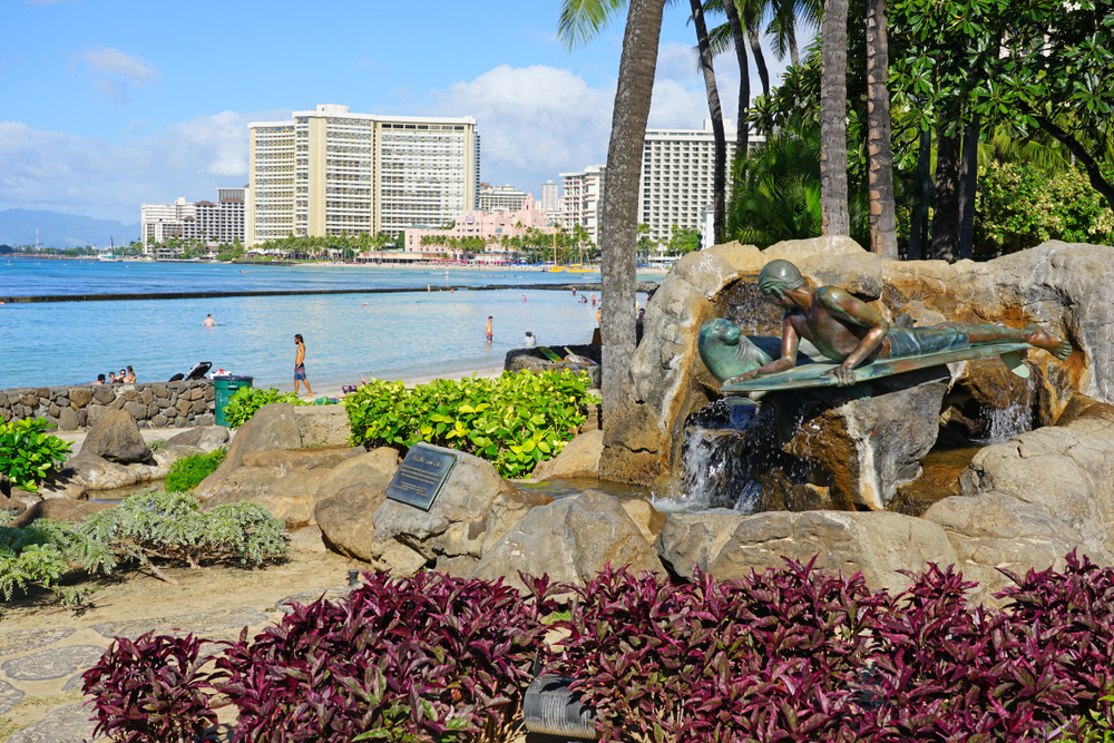 People walking on the beach with rocks and hotels all around in Waikiki, pictured for a piece answering the question, 