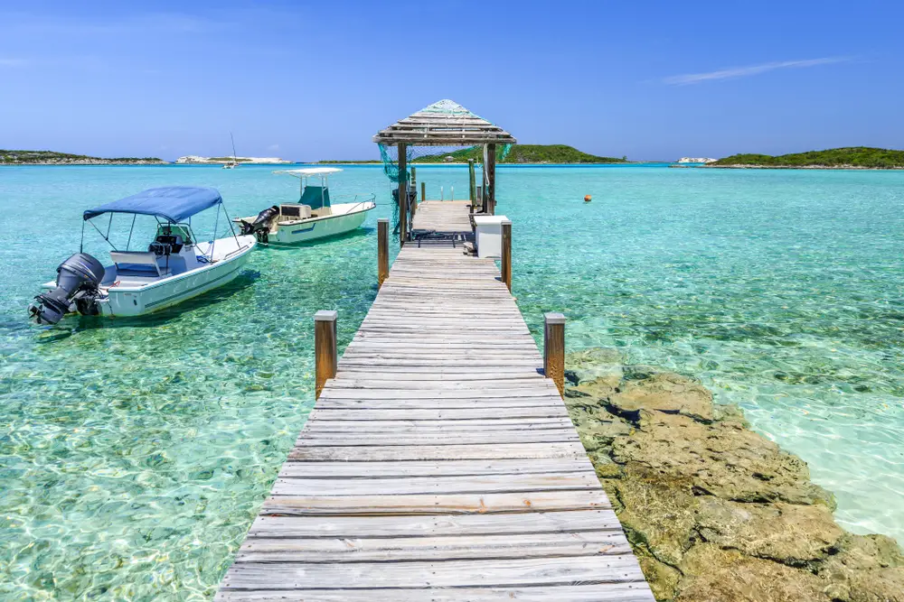 Wooden pier near Staniel Cay in Exuma, one of the safest areas in the Bahamas, pictured on a clear day with teal water below the boat floating on the water