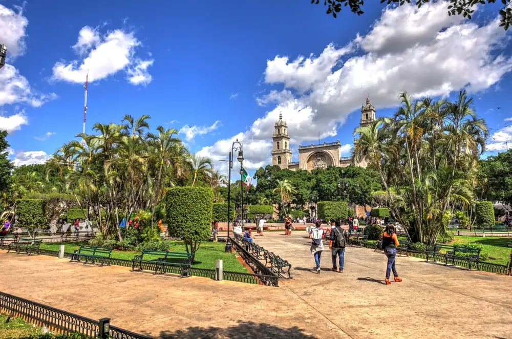 People walking around a park in Merida, Mexico, during the overall best time to visit with blue skies and green trees in a well-manicured park in the historical city center