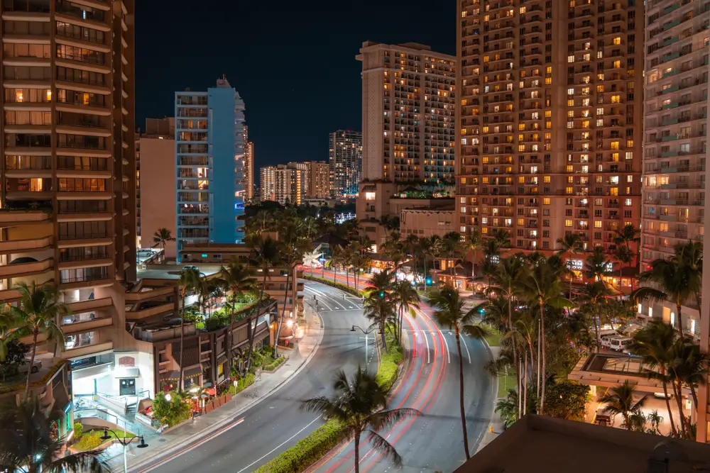 Neat view of downtown Honolulu at night as seen from a tenth story window with cars whizzing by below for a piece titled is Honolulu safe to visit