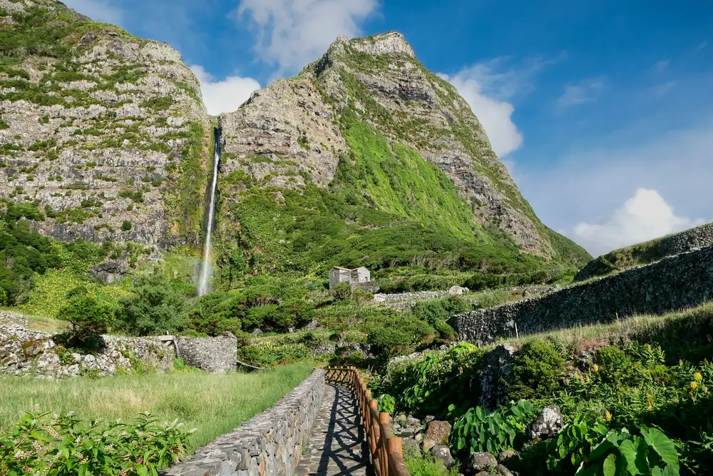 Waterfall towering high above the brick walking path and surrounded by greenery for a piece titled Are the Azores Safe to Visit