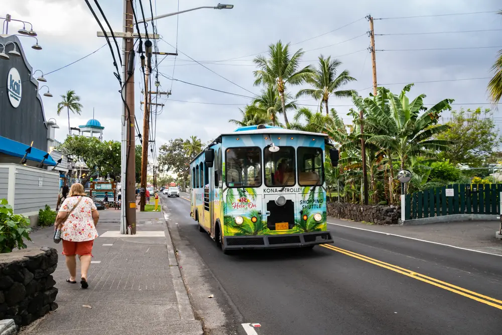 Multi-colored bus driving down the street on Ali'i Drive in downtown Kona for a guide to whether or not it's safe to visit the island