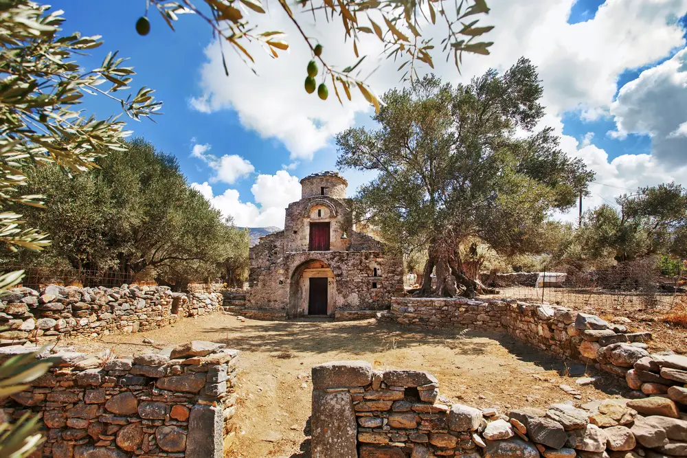 For a guide to the best areas to stay in Naxos, the Agii Apostoli Byzantine with olive trees sits abandoned behind a stone wall
