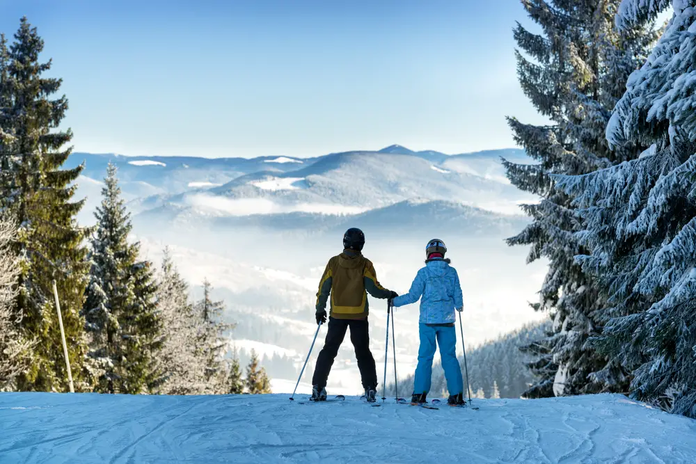 A look at one of the best couples vacations in the US, with the concept of skiing at Park City, Utah as a couple holds hands before going down the slope
