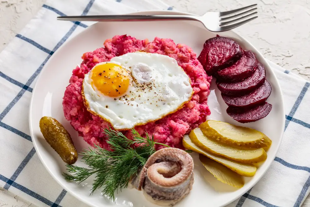 Labskaus dish with corned beef, beets, and potatoes served with beets, sausage, fish, and pickles topped with a fried egg might be the best German food to try