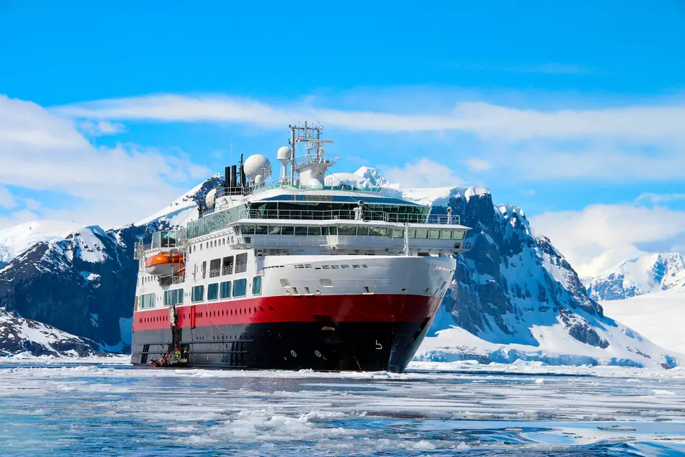 Ασπρόμαυρο κρουαζιερόπλοιο που απεικονίζεται να επιπλέει στον ωκεανό με έναν παγετώνα στο φόντο για ένα κομμάτι με τίτλο Τι κοστίζει ένα ταξίδι στην Ανταρκτική;