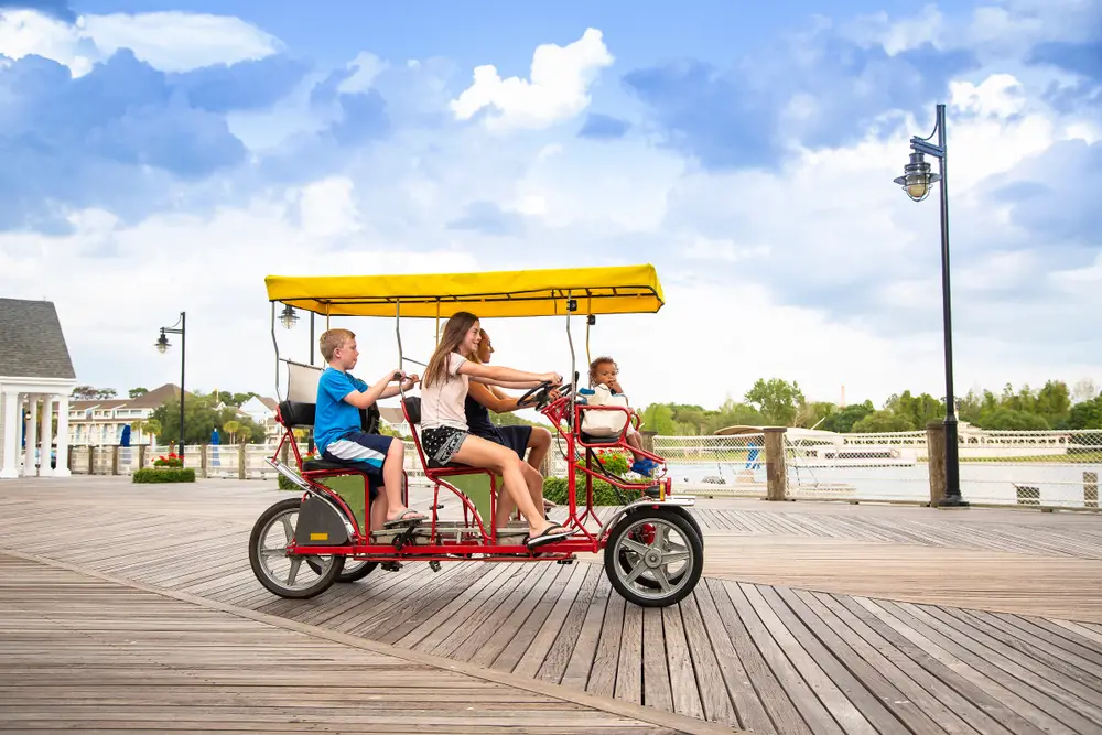 Family riding in a covered tandem bicycle on a boardwalk to show the concept of a family vacation in Orlando, Florida