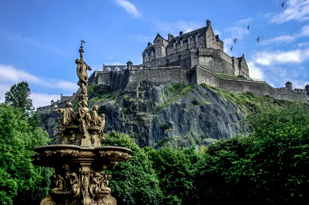 Edinburgh Castle in the capital of Scotland with a fountain in the foreground during summer shows one of the top bucket list travel ideas