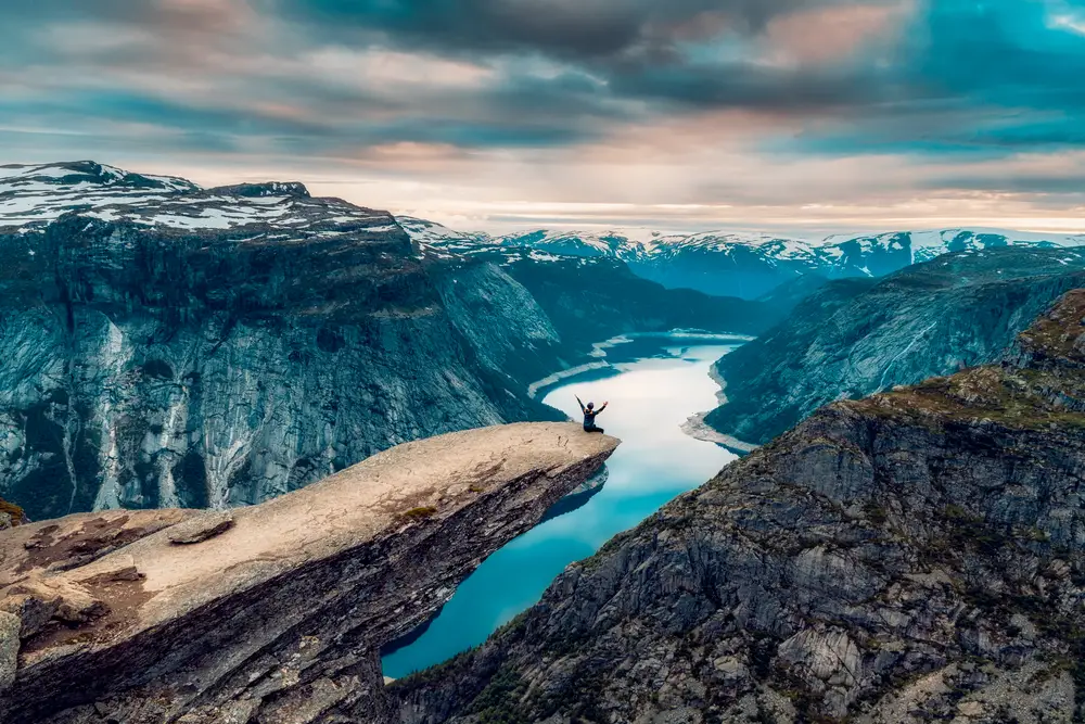 Man sits on a cliff over Trolltunga over Ringedalsvadnet as an image for a guide to the average Norway trip cost