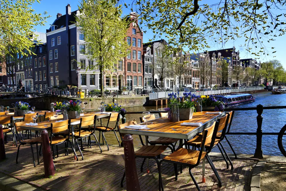 Restaurants with outdoor tables lining a railing for a guide to the average trip to Amsterdam cost