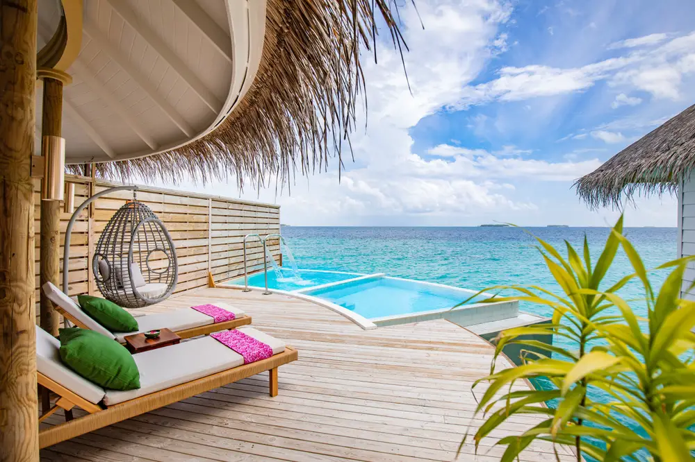 View from the deck of an overwater bungalow with pools, deck chairs, thatched roof, and plants over the ocean to show what accommodations look like at the best honeymoon destinations