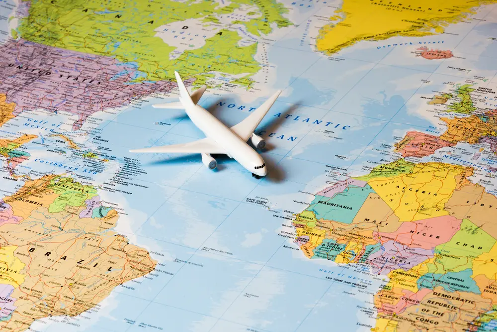 Map of the world shown close-up with a white model airplane resting on it between the United States and Africa to indicate how to use Google Flights to book flights for a trip anywhere