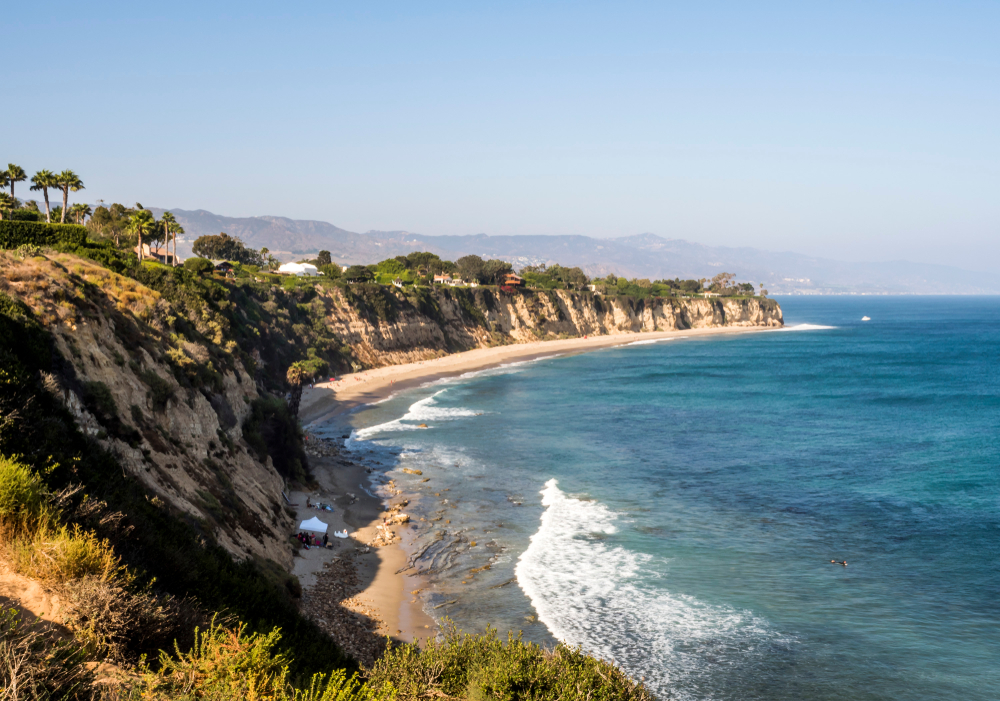 Paradise Cove Beach in Zuma, Malibu, CA ranks as one of the best beach vacations in the US, shown from an aerial view with cliffs and waves crashing on the sand