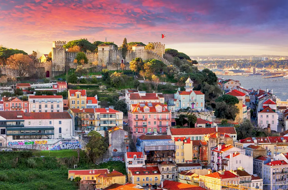Skyline view of Lisbon, Portugal at sunset with colorful Baroque buildings on the coast for a list of the best cities to visit in Europe