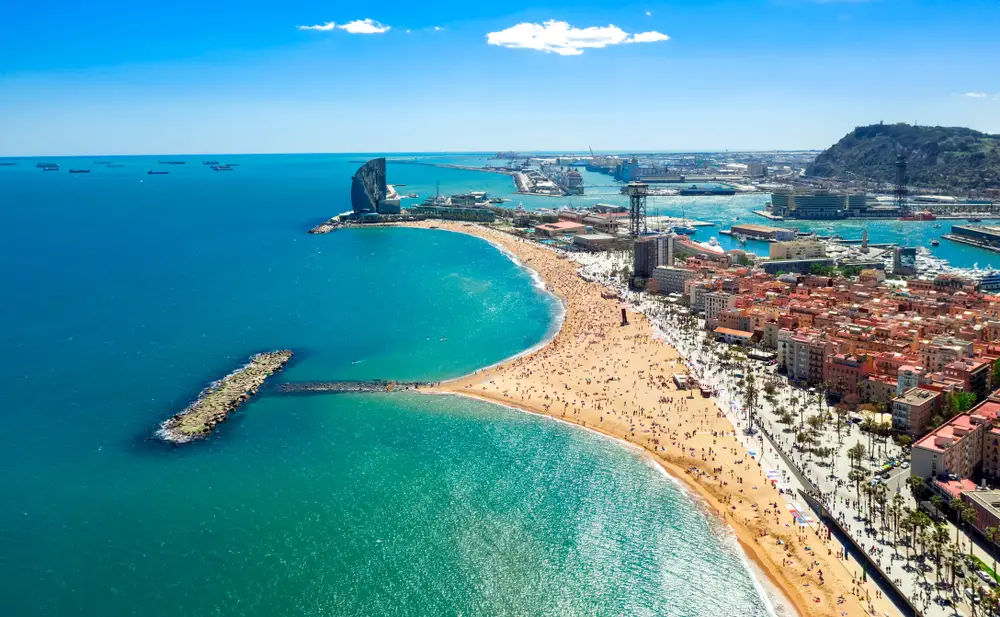 Barcelona beach Sant Sebastian shown with an aerial view during busy season with mostly clear skies overhead to show one of the best tourist destinations worldwide