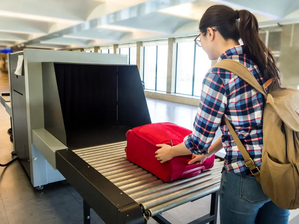 Airport traveler woman sends her red luggage through an X-ray machine for customs to show part of the process for people wondering What is customs at the airport?
